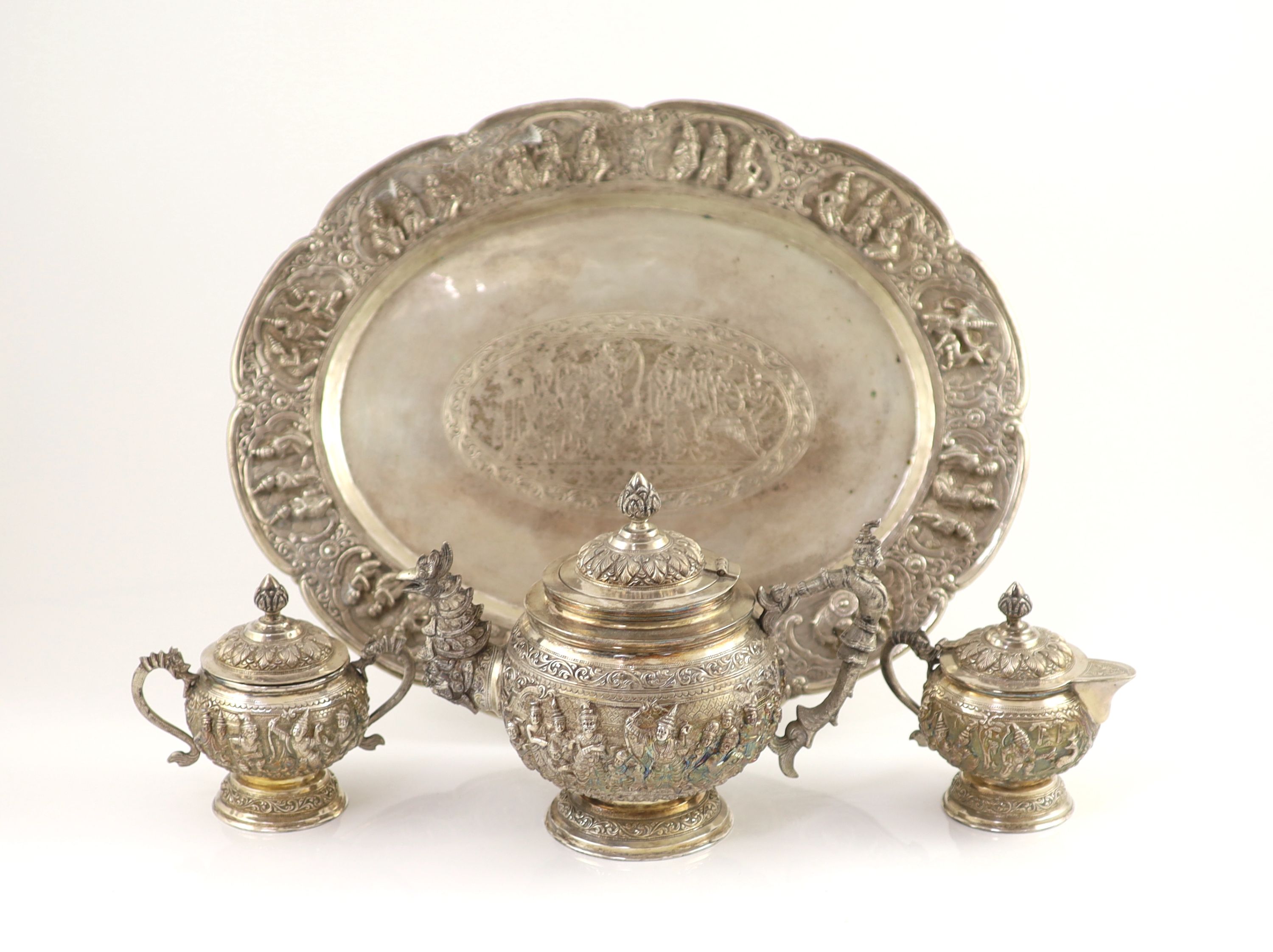 An impressive Burmese Sterling silver (950) three-piece tea service, with tray, cast with figures, teapot with cockerel spout and figural handle